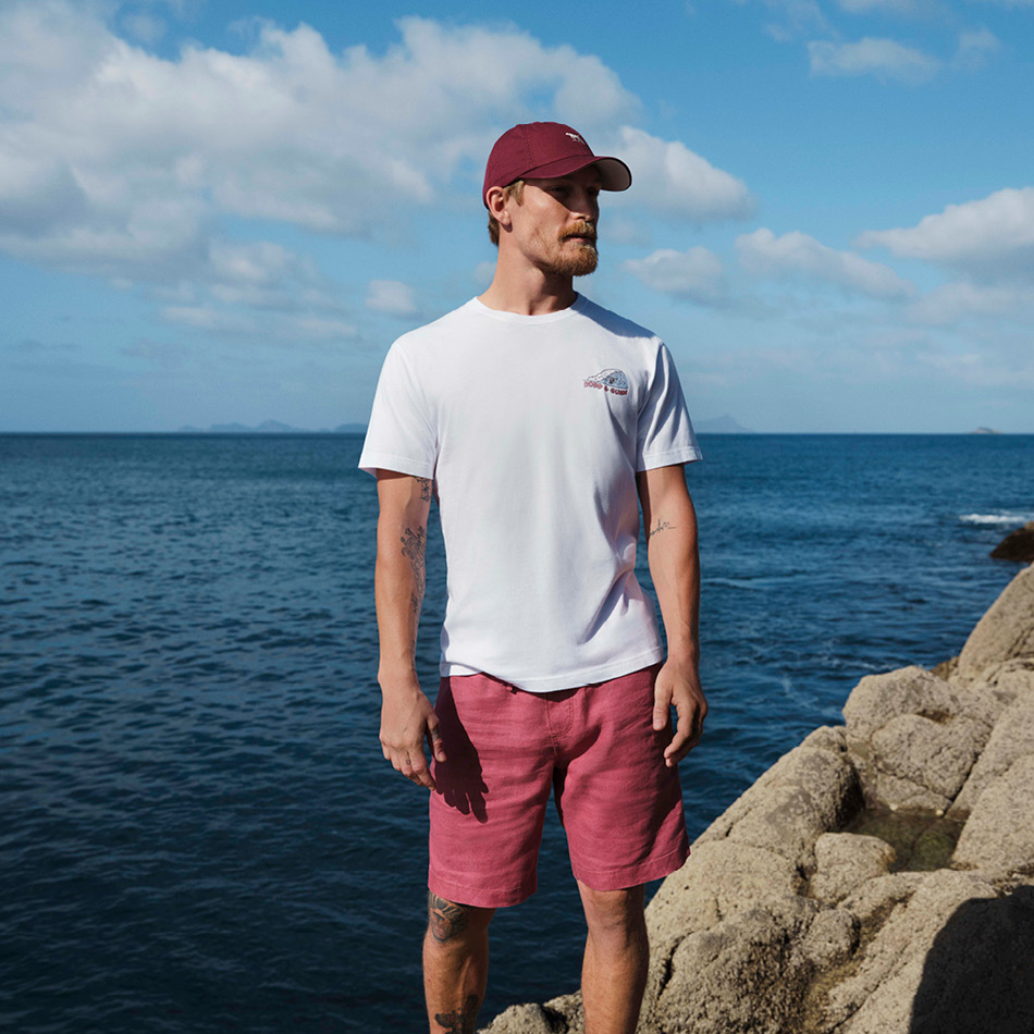 Man standing by the ocean wearing a white t-shirt and red shorts.