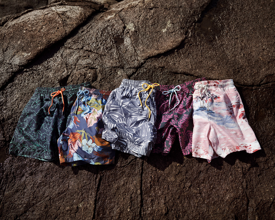Swim shorts lined up on display on a rock by the ocean.
