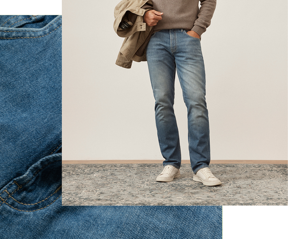 Man sitting on stool wearing dark denim jeans and jacket and scarf.