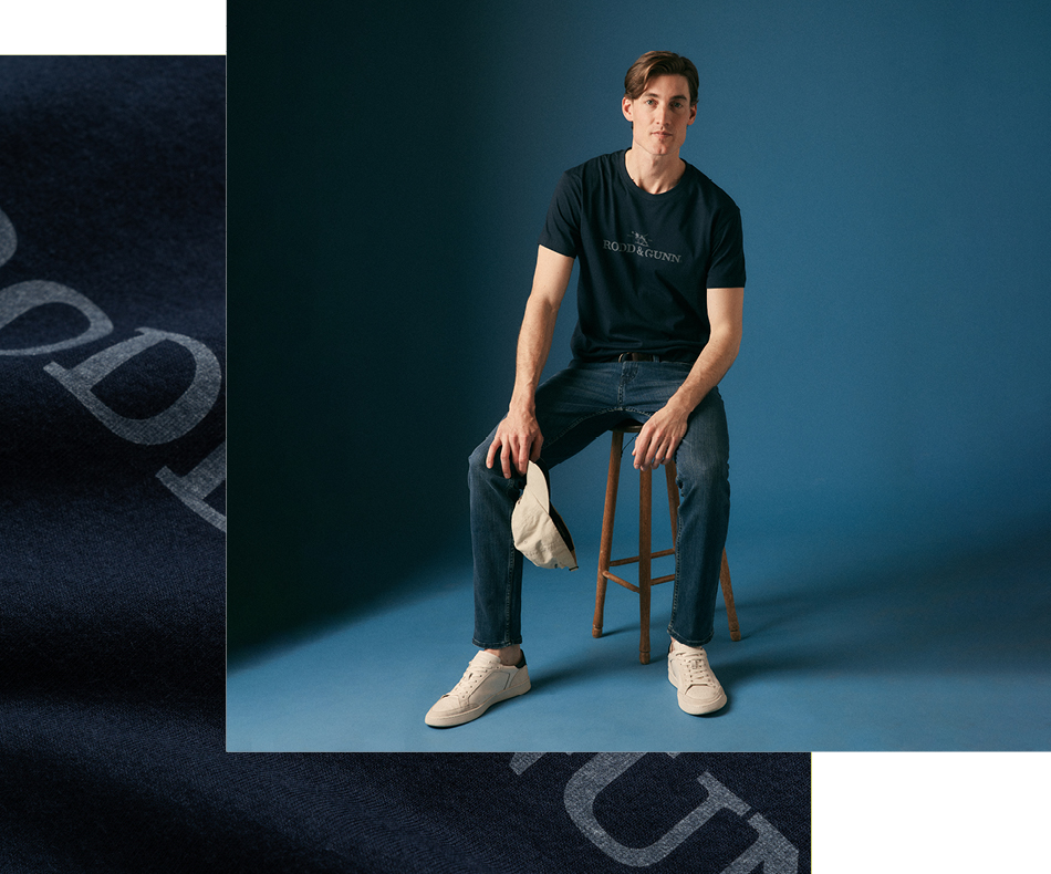 Man sitting on stool wearing dark denim jeans and jacket and scarf.
