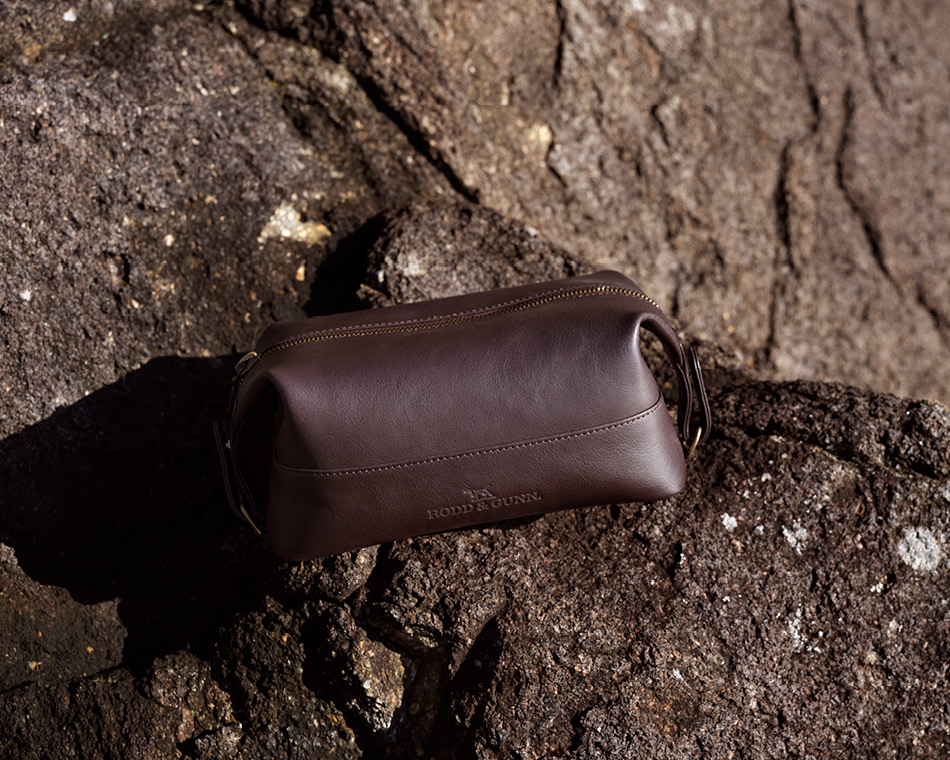 Brown leather shave bag sitting on rocks by the sea.